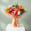 Large bouquet of orange lilies, pink roses, and white daisies wrapped in peach paper