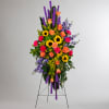 Tall standing floral spray with sunflowers, roses, and purple flowers on an easel