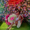 Woman seated on a pink sofa holding a bouquet against a flower wall