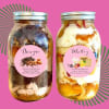 Two dessert jars with layered cake and frosting on a pink background
