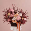 Pink and peach floral arrangement in a wicker basket with ribbon