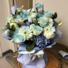 Blue and white bouquet of roses, daisies, and hydrangeas wrapped in lavender paper