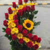 Red roses and yellow daisies arranged with a sunflower
