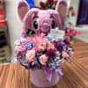 Pink plush bunny holding a mixed bouquet in a round box