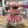 Tiered arrangement of pink roses with white baby's breath in a white container