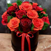 Red and orange roses arranged in a black round box with a red ribbon