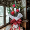 Tall bouquet of red roses with decorative greenery and a plaid ribbon