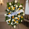 Standing floral wreath of white and yellow roses with a memorial ribbon