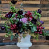 Purple and burgundy floral arrangement in a white pedestal vase