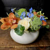 Orange orchids and a white rose in a white bowl vase