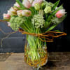 Pink and white tulips arranged in a glass vase with curly branches