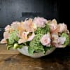 Low floral arrangement of pale pink orchids and ruffled pink blooms in a white bowl