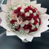 Round bouquet of red and blush roses with baby's breath in pink wrapping paper.