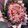 Bouquet of pink and red roses with purple filler flowers, wrapped in pink paper with a jeweled tiara and letter A.