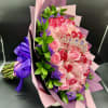 Bouquet of pink and red roses with purple filler flowers, wrapped in pink paper with a small tiara decoration.