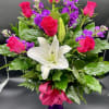 Arrangement of hot pink roses, purple stock, and white lilies in a purple vase with a pink bow