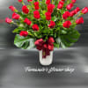Tall arrangement of red roses in a white vase with large glossy leaves and a red ribbon bow