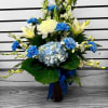 Tall blue and white flower arrangement with lilies, carnations, and hydrangea in a vase with a blue ribbon