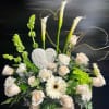 Tall white and green sympathy arrangement with roses, calla lilies, and angel plaque in a stone urn.