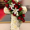 Tall white floral cross with red roses and white lilies accenting the upper side