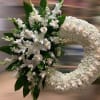 Large white funeral wreath with roses and lilies clustered on one side of the ring