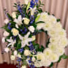 Standing white and blue sympathy wreath with lilies, roses, and mums on an easel