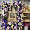 Standing rectangular wreath of pink, purple, yellow, and white flowers with ribbons on an easel