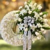 Large white floral wreath with side spray of lilies and roses on a standing easel with a printed ribbon