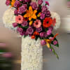 Standing white floral cross with cluster of purple roses, orange lilies, and pink gerberas.