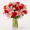 Tall clear vase of red roses and pink lilies arranged in a rounded bouquet