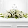 Low white floral spray with lilies and roses accented by a clear cross ornament.