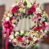 Standing wreath of pink, white, and peach flowers with a bright pink ribbon bow on an easel.