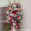Tall standing spray of pink, white, and peach flowers with a pink ribbon on an easel