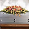 Peach and yellow casket spray of roses and mixed blooms with ribbon on a silver casket