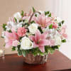 Pink lilies, white roses, and mixed blooms arranged in a wicker basket on a wooden table