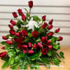 Fan-shaped arrangement of red roses with a white Jesus figurine and red ribbon loops