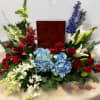 Red, white, and blue sympathy arrangement surrounding a wooden urn on a draped table