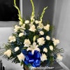 Tall white and blue floral arrangement with roses, lilies, and carnations in a container with a blue bow