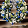 Round wreath of blue and white flowers with green accents and a printed memorial ribbon bow