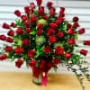 Large fan-shaped arrangement of red roses in a clear glass vase with a red bow.