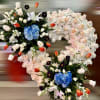 Heart-shaped standing spray of white roses with blue hydrangea clusters and orange tulips.