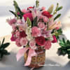Pink and red bouquet with lilies, roses, and carnations in a painted ceramic vase with a pink bow.