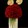 Tall cream vase filled with a dome of red roses, trailing greenery, and three gold anthurium stems
