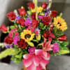 Tall mixed arrangement with red roses, sunflowers, pink lilies, and carnations in an orange pot with a pink bow.