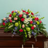 Large casket spray of red carnations, white lilies, pink roses, green blooms and blue delphinium