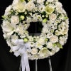 Standing white funeral wreath of roses, lilies, and chrysanthemums with a bow on a metal easel