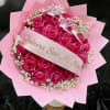 Bouquet of bright pink roses with baby's breath, pink wrapping, and a ribbon with Spanish proposal text