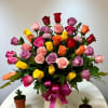 Colorful bouquet of roses in a white vase with a pink ribbon
