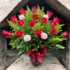 Red roses and pink pompom flowers in a patterned vase with a burgundy ribbon