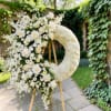 White floral wreath on a wooden stand with roses and small blooms